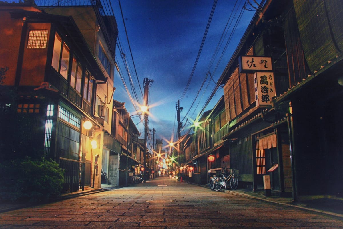 Lantern-lit wooden buildings along a quiet street in Gion, Kyoto, at dusk.
