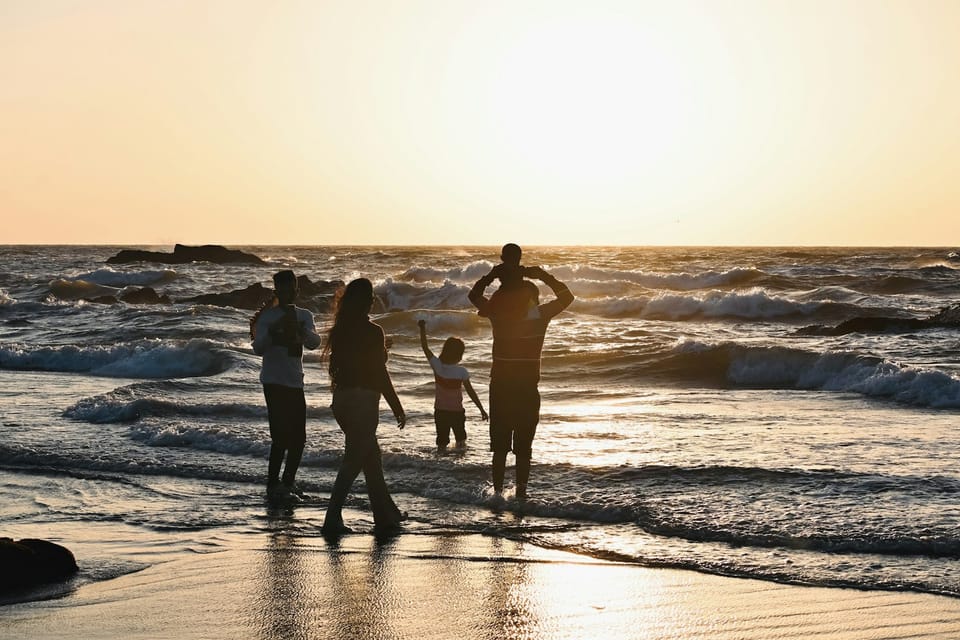 A family silhouetted against golden waves on a beach at sunset.